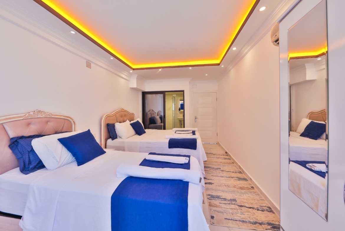 İki yataklı geniş yatak odası, beyaz duvarlar ve mavi detaylar.