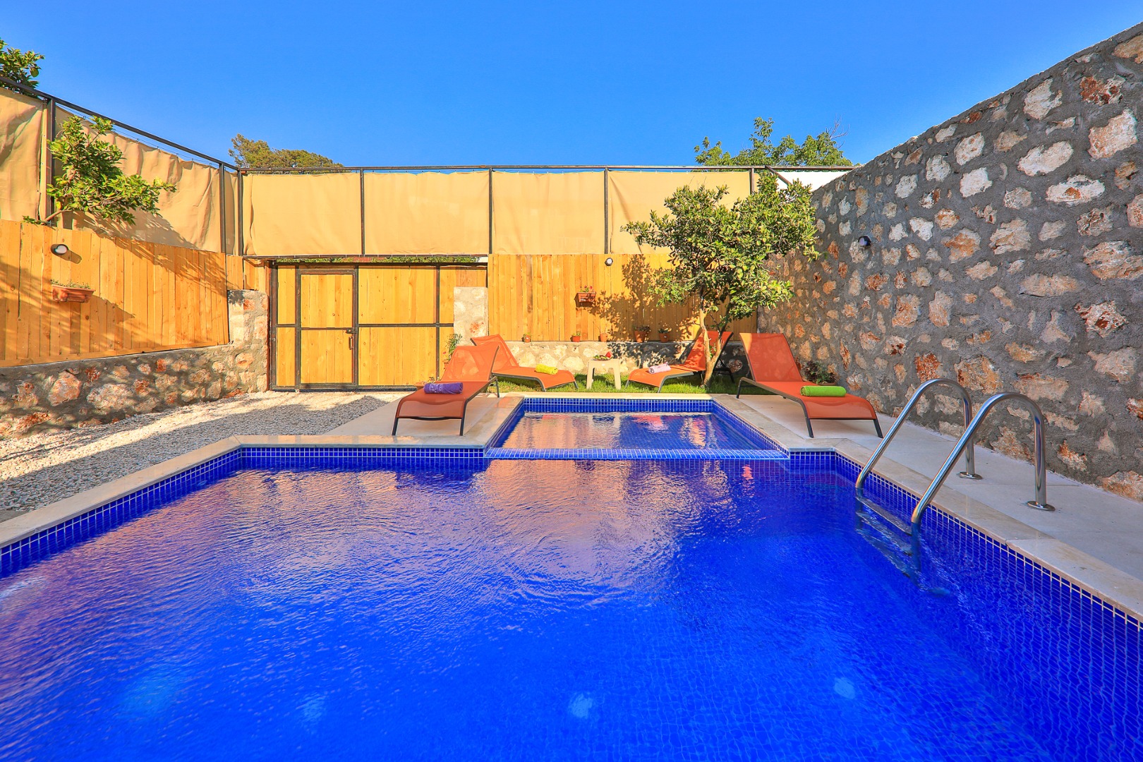 Taş duvarlı bahçede mavi seramik kaplı yüzme havuzu.